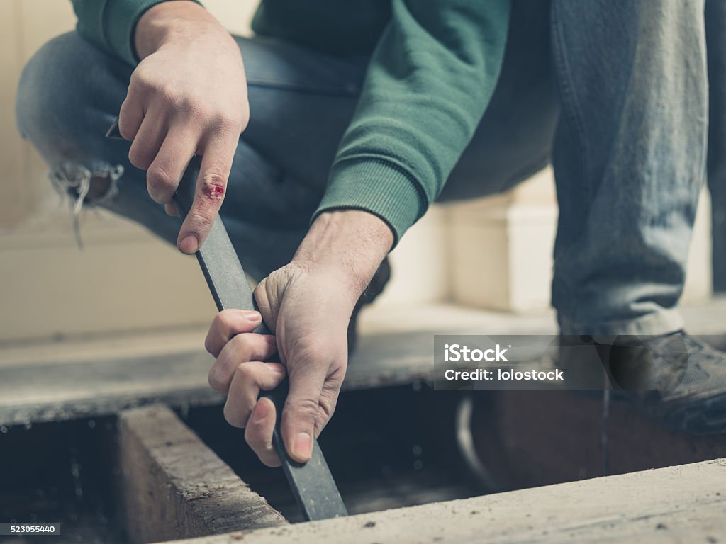 Injured man using a crowbar on floor boards A young man with an injury to his hand is using a crowbar to remove a floor board Floorboard Stock Photo