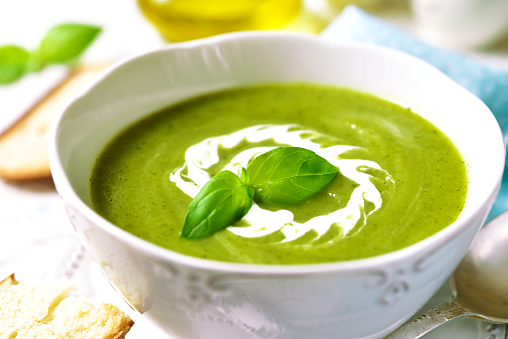 Zucchini creamy soup with basil on a light background.