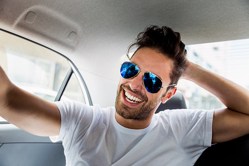 A photo of young man wearing sunglasses. Attractive young male is enjoying road trip in car. He is wearing casuals.