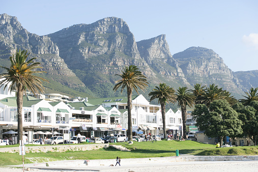 Camps Bay, South Africa - October 23, 2014: The promenade of Camps Bay at the atlantic ocean close to Cape Town in South Africa. In the back you can see mountains of the famous Twelve apostels. In the front people are strolling down the promenade which is famous for its restaurants.
