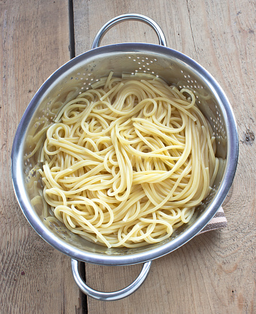 Fresh cooked spaghetti in strainer on wooden table