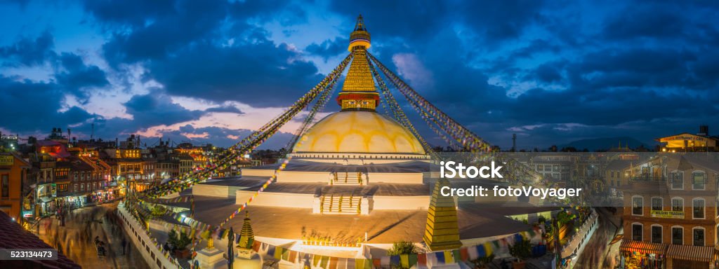 Prayer flags Buddhist stupa illuminated panorama at Boudhanath Kathmandu Nepal The iconic mandala dome of Boudhanath stupa, illuminated by spotlights under colourful prayer flags fluttering in the evening breeze as crowds of pilgrims and tourists walk around the ancient Buddhist shrine, a UNESCO World Heritage Site in Kathmandu, Nepal's vibrant capital city. ProPhoto RGB profile for maximum color fidelity and gamut. Bodnath Stupa Stock Photo