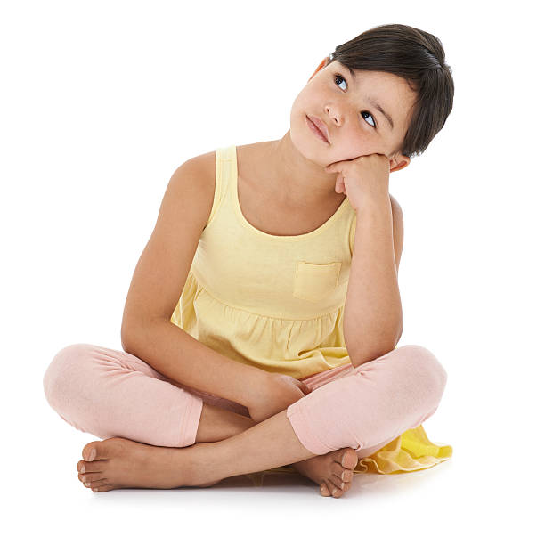 Shot cute little girl daydreaming while sitting cross-legged in studio