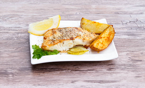 White fish White fish with potato wedges, lemon and celery on white plat, wooden background freshwater bass stock pictures, royalty-free photos & images