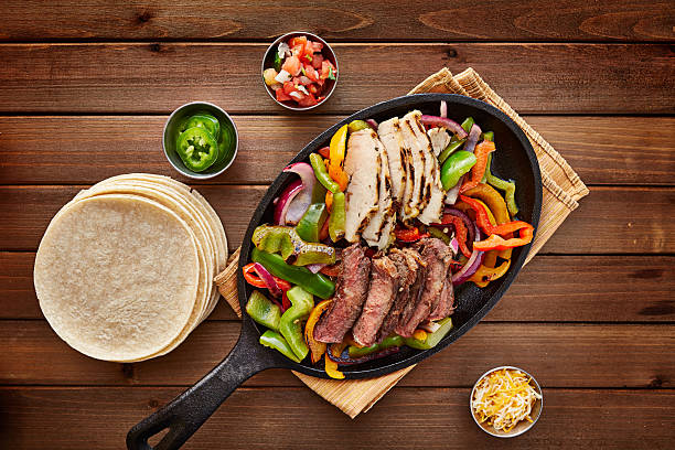 mexican steak and chicken fajitas over head photo mexican steak and chicken fajitas in cast iron skillet shot top down with corn tortillas salsa music photos stock pictures, royalty-free photos & images