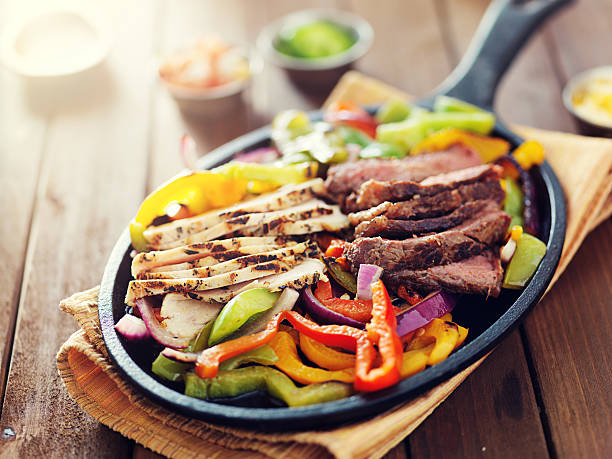 mexican food - skillet fajitas with steak and chicken skillet fajitas with steak and chicken on rustic wooden table with lens flare fajita photos stock pictures, royalty-free photos & images