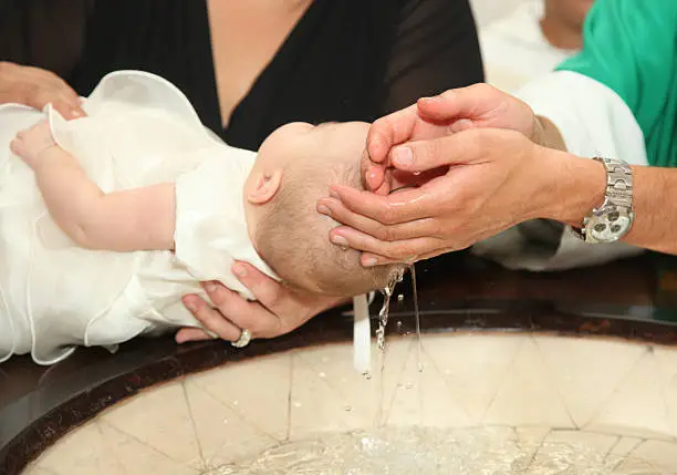 Newborn baby baptism by water with hands of priest