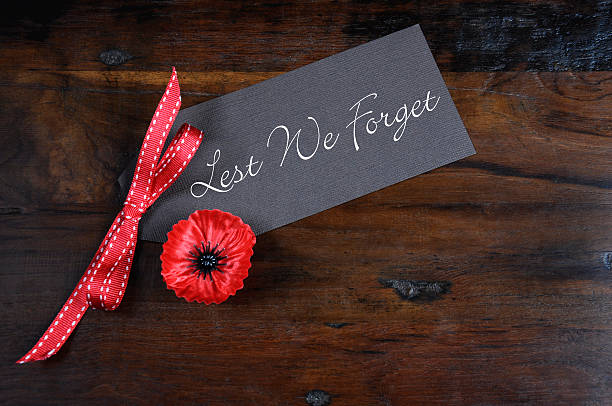 Lest We Forget Red Poppy Lapel Pin Badge Lest We Forget, Red Flanders Poppy Lapel Pin Badge for November 11, Remembrance Day appeal, on dark recycled wood background. corn poppy photos stock pictures, royalty-free photos & images