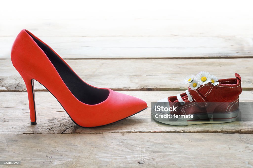 red kids sneakers with daisies and mum's red high heels red kids sneakers with a bouquet of daisies and mum's red high heels on rustic wooden planks, concept for mother's day, background fades to white Child Stock Photo