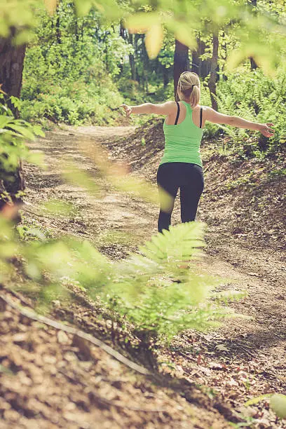 Young blonde caucasian woman running in the forest; outdoor sport photography, all logos removed.