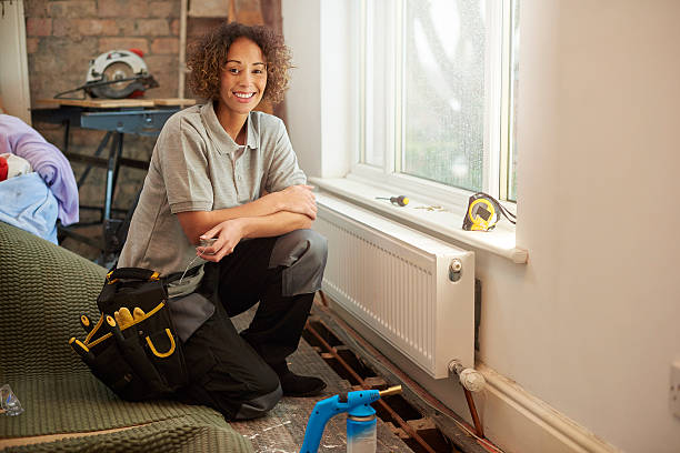 female plumber on site a mid adult female plumber is installing a new radiator into a property undergoing refurbishment. The floorboards are raised with new paperwork shown , and she is soldering a copper pipe join .She is wearing work trousers , and tool belt . In the background more work tools can be seen as is an exposed brick wall . Plumber stock pictures, royalty-free photos & images