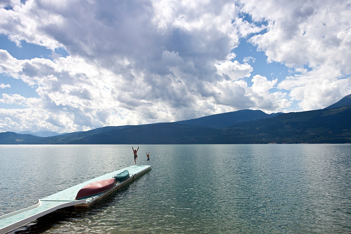 A man and child jumping off a dock on a beautiful mountain lake.