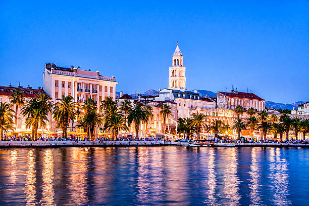 Magical Cityscape of old town Split, Croatia at Dusk Magical Cityscape of old town Split, Croatia at Dusk with his historic buildings. Visible are sailing boats, Diocletian Palace, city lights, restaurants, coffee bars, hotels and many palm trees. Beautiful night scene with blue sky and their reflection in the water.   split croatia stock pictures, royalty-free photos & images