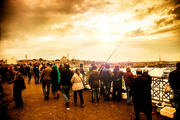 Istanbul cityscape at dusk exterior view of Yeni Camii from Galata Bridge, blurred fishermen on foreground.
