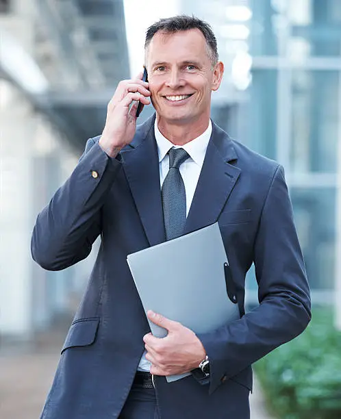 Portrait of a businessman talking on his mobile phone while holding a file in the other hand