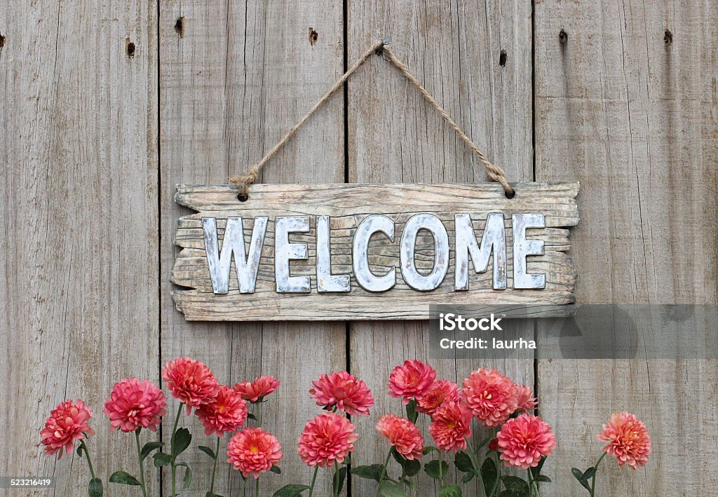 Wood welcome sign with autumn flower border by wooden background Rustic antique wooden welcome sign with pink mums hanging on old weathered fence Welcome Sign Stock Photo