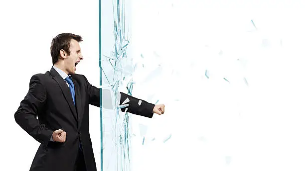Young determined businessman breaking glass with karate punch