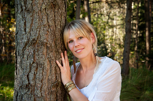 Ecology and environment-Portrait of white woman  embracing and hugging tree in a forest, smiling and looking at camera