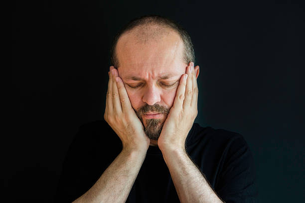 istock Adult man on black background, eyes closed, having headache 523244488