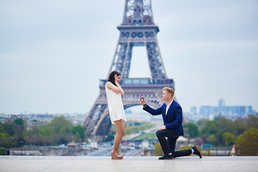 Romantic engagement in Paris, man proposing to his beautiful girlfriend near the Eiffel tower. Surprise proposal or elopement concept