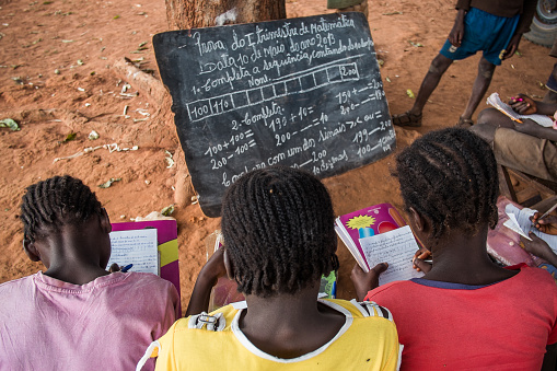 Bie, Angola - May 10, 2013. Three girls undertake a maths exam by a tree in a rural school. Access to education in low income countries of sub-saharan Africa is one of the challenges of the global community, as stated in the Sustainable Development Goals. 