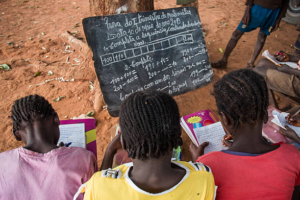 The maths test Bie, Angola - May 10, 2013. Three girls undertake a maths exam by a tree in a rural school. Access to education in low income countries of sub-saharan Africa is one of the challenges of the global community, as stated in the Sustainable Development Goals.  africa school stock pictures, royalty-free photos & images