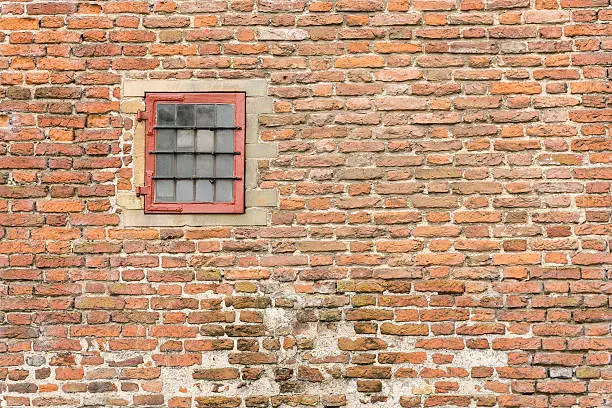 Old fortress wall with a frame and a turn window with glass rods.