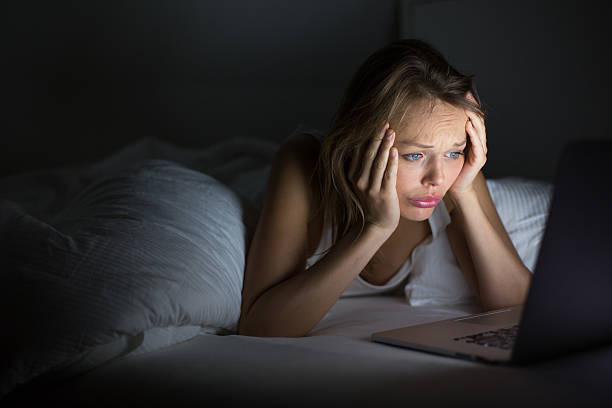 Pretty young woman watching on her laptop Pretty young woman watching something awful or sad on her laptop in bed at night in a dark bedroom (shallow DOF; color toned image) ugly people crying stock pictures, royalty-free photos & images