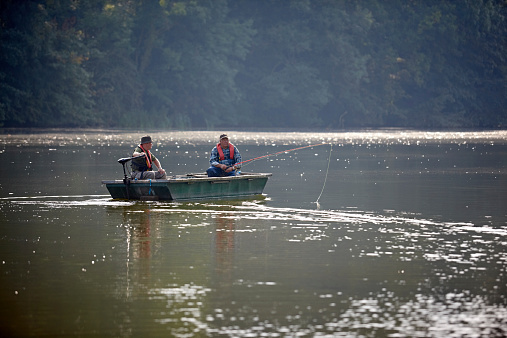 Image of two senior men fishing from a small boat on lake