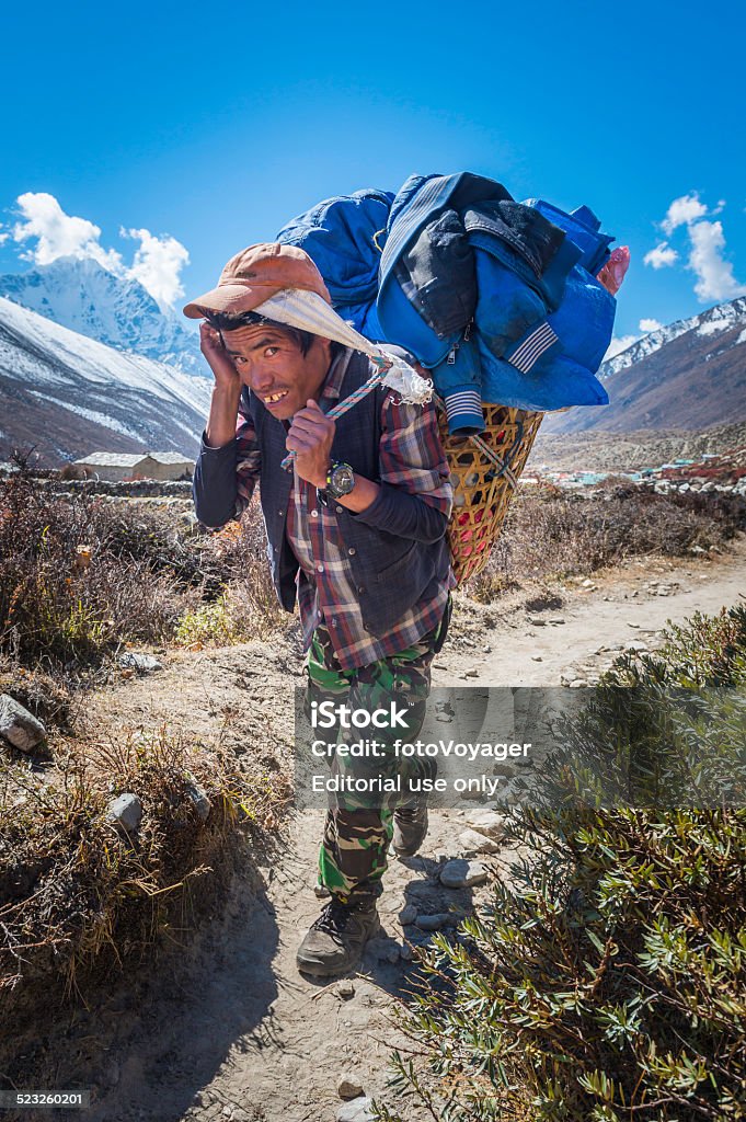 Sherpa porter carrying heavy basket along trail Himalayas Nepal Dingboche, Nepal - 24th October 2014: Sherpa porter carrying traditional wicker basket with head band along an earth trail deep in the high altitude Himalaya mountains of the Sagarmatha National Park, Nepal, a UNESCO World Heritage Site.  Adult Stock Photo