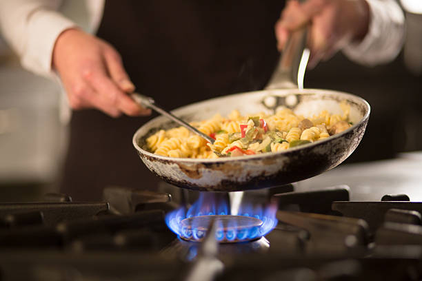 Pasta dish with vegetables on stove Female cook preparing pasta dish with vegetables on stove stove stock pictures, royalty-free photos & images