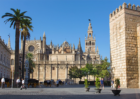 Seville, Spain - October 29, 2014: Cathedral de Santa Maria de la Sede with the Giralda bell tower and walls of Alcazar and mumber of peoples on the square.