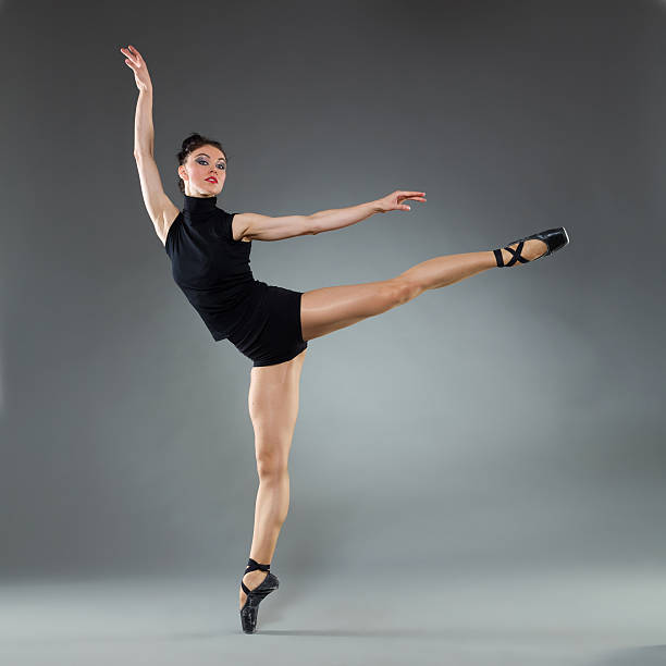Ballet pose Female ballet dancer is posing on one leg with arms outstretched. Full length studio shot on gray background. jazz dancing stock pictures, royalty-free photos & images