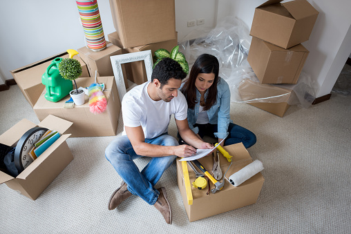 Latin couple moving house and packing in boxes while looking at checklist