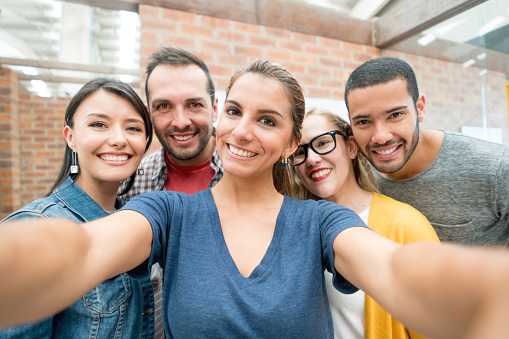Group of people taking a selfie at the office with a cell phone looking very happy