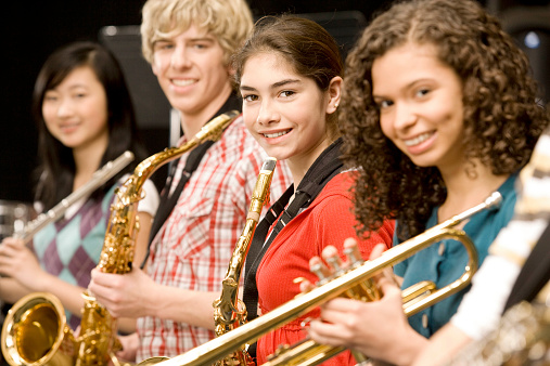 Woman playing a sax and two men in the back playing a trombone and a cello isolated on white background