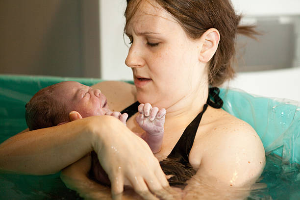 Mother Holding Newborn in Birthing Tub After Home Water Birth Color photo of a loving mother holding her newborn baby son in the water of a birthing tub immediately after a water birth at home. water birth stock pictures, royalty-free photos & images