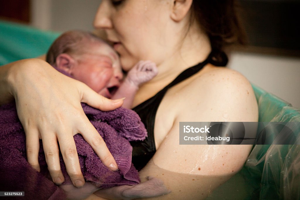 Mother Holding Newborn in Birthing Tub After Home Water Birth Color photo of a loving mother holding her newborn baby son in the water of a birthing tub immediately after a water birth at home. Water Birth Stock Photo