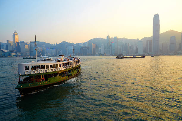 Kowloon, Hong Kong - November 25, 2010: Evening approaches in Hong Kong, and one of the city's iconic Star Ferries sets out from the ferry terminal at Tsim Sha Tsui, ready to cross Victoria Harbour. The modern skyscrapers of Hong Kong Island loom in the background.