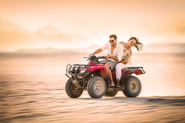 couple sur un quad vélo au coucher du soleil. - off road vehicle quadbike desert dirt road photos et images de collection