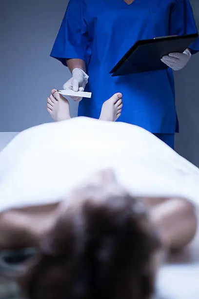 Worker of morgue labeling of corpse of young woman