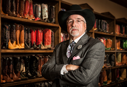 Portrait of a mature business owner standing in front of a wall of cowboy boots.