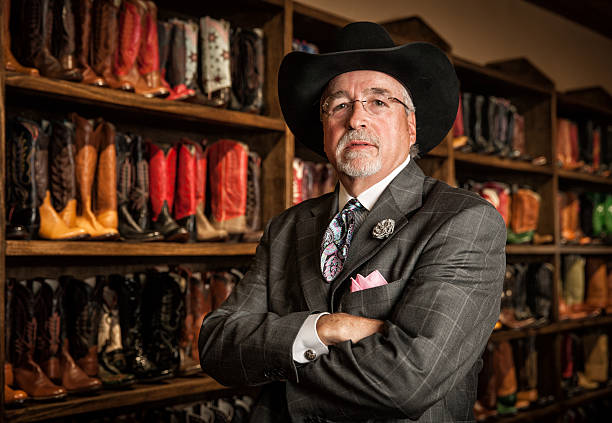 Cowboy Boot Store Owner Portrait Portrait of a mature business owner standing in front of a wall of cowboy boots. texas cowboy stock pictures, royalty-free photos & images
