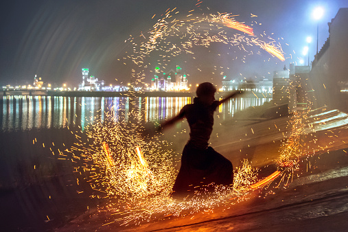 Young man dancing with flame at night on embankment of city. Shot with using a long exposure