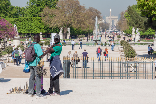 Paris, France - April 25, 2013:Black man souvenirs seller in Jardin des Tuileries in Paris. In background Jardin des Tuileries Garden.