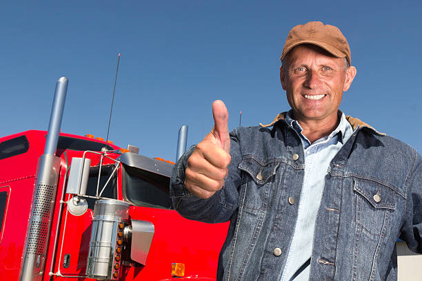 A royalty free image from the trucking industry of a positive truck driver giving the thumbs up in front of his red semi truck.