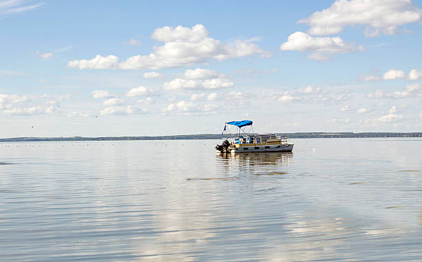large pontoon boat coasting on a very big lake. horizontal image of a pontoon boat coasting on a beautiful blue lake under clear blue sky in the summer time. pontoon boat stock pictures, royalty-free photos & images