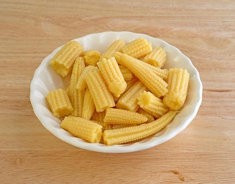 A small bowl of corn nuggets atop a wood table.