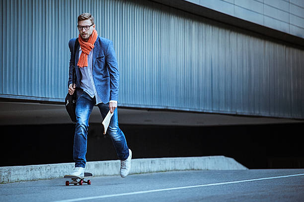 Young casual businessman comuting to work skateboarding.
