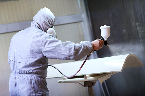 Mechanic in Painting Booth Spray Wooden Part of Furniture or hood of a car.